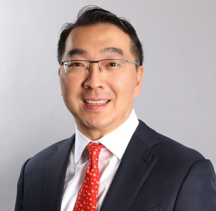 Jay Koh smiles in a black suit, white shirt and red tie.