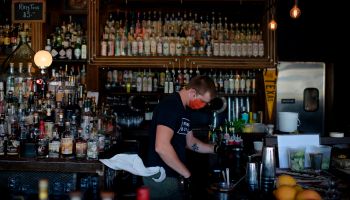 A bartender wearing a face mask and gloves makes drinks.