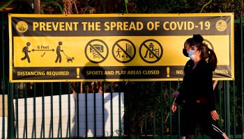 Pedestrians wearing face masks walk past a "Prevent the spread of COVID-19" banner in Los Angeles on Jan. 19.