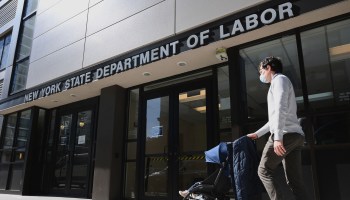 A man pushes a stroller past the New York State Department of Labor office in Brooklyn, New York.