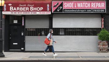 A woman walks by a closed barber shop and shoe and watch repair store in the Brooklyn borough of New York City.
