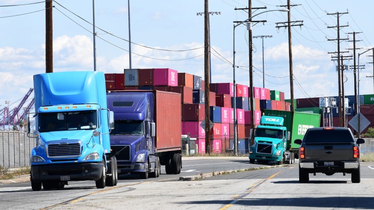 Trucks drive past stacked containers at the Port of Los Angeles. The industry is having problems recruiting and retaining enough qualified drivers.