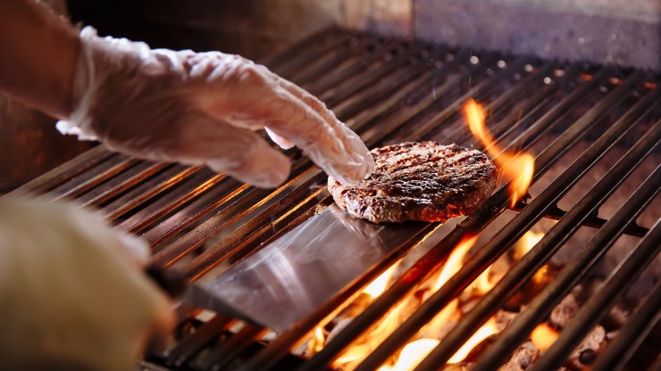 A line cook flips a burger on a grill.