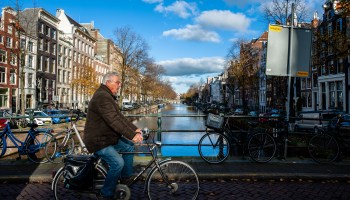 A cyclist rides down the street in Amsterdam next to a canal.