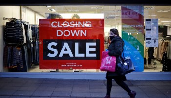 A shopper wearing masks because of the COVID-19 pandemic walks past a "Closing Down" sale sign in the window of a Peacocks clothing store in Walthamstow, northeast London, on December 15, 2020.