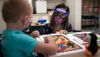 A teacher wearing a face mask and shield helps a first grader during reading class at an elementary school in Stamford, Connecticut, on September 16, 2020.
