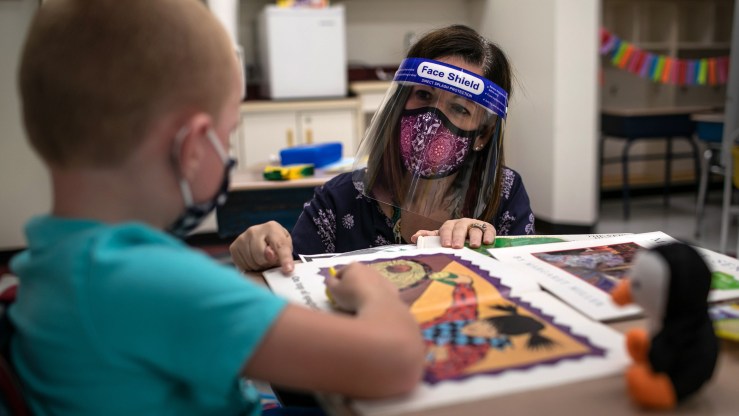 A teacher wearing a face mask and shield helps a first grader during reading class at an elementary school in Stamford, Connecticut, on September 16, 2020.