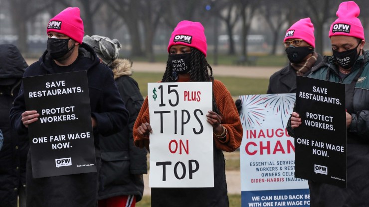 Service industry workers listen to remarks and hold up signs during a rally at the National Mall on January 26, 2021 in support of the introduction of the Raise the Wage Act, which includes a $15 minimum wage for tipped workers and is also included in President Biden's American Rescue Plan.