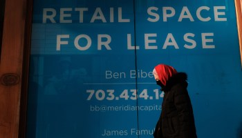 A woman walks through a Manhattan neighborhood on February 5, 2021 in New York City. Behind her is a sign on a building advertising retail space for lease.