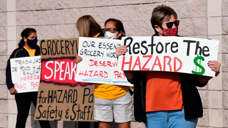 Supermarket workers hold signs demanding the restoration of hazard pay.