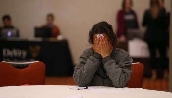 A woman covers her face, pausing while filling out a job application.