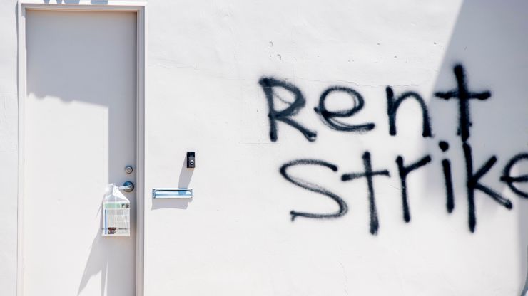 Graffiti calling for a rent strike against a white wall.