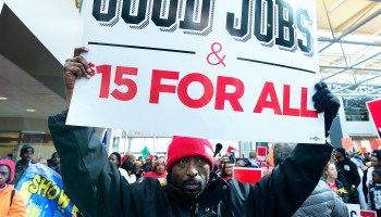 A protester holds up a sign calling for "$15 minimum wage for all."