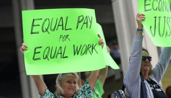 A woman holds up a sign saying "Equal Pay for Equal Work."