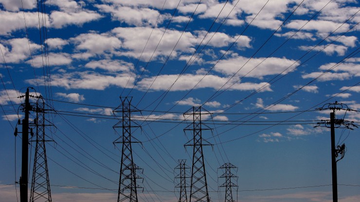A line of electricity transmission towers under a blue sky.
