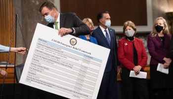 A U.S. senator places a poster describing a proposal for a COVID-19 relief bill alongside a bipartisan group of Congress members.