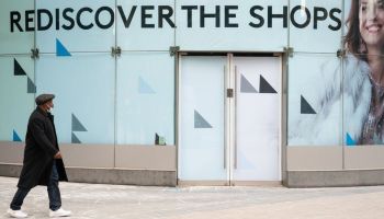 A shopper walks past a sign reading "Rediscover the shops" in London, England.