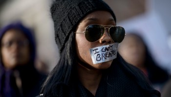 A Black woman listens to a rally with her mouth taped over with the words "I can't breathe."