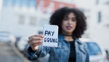 A woman holds up a notepad that reads "Pay Equal."