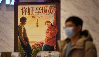 A man walks past a poster for the movie "Hi, Mom" at a cinema in Beijing on February 20, 2021.