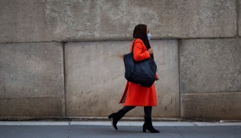 A woman in a red coat and black tote bag walks in New York's financial district.