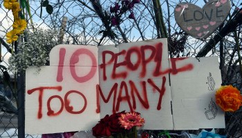 A sign reading "10 People Too Many" along with flowers hang from the perimeter fence outside a King Soopers grocery store in Boulder, Colorado on March 24, 2021, to honor the 10 people killed during a mass shooting at a King Soopers grocery store.
