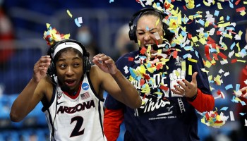 A college basketball player and head coach are showered in confetti after a win.