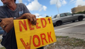 A man holds a sign reading "Need work."