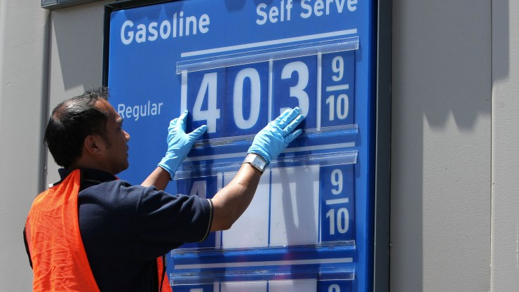 An employee changes the price on a gas station sign to represent the new price.