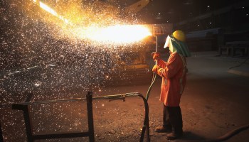 A steel worker trims newly cast steel.