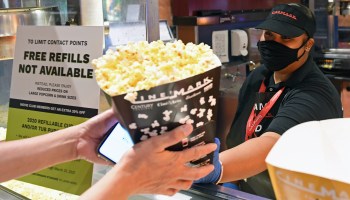 A movie theater worker serves popcorn to a customer.