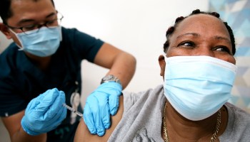 A woman smiles behind her mask as a nurse gives her the COVID-19 vaccine.