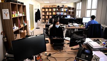A woman wearing a protective facemask works in a mostly empty office.