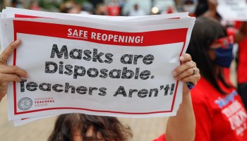 A woman holds up a sign reading "Masks are disposable. Teachers Aren't!"