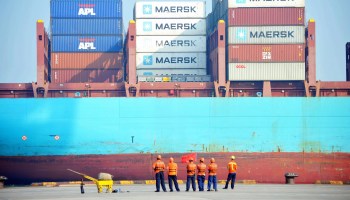 Workers looks as a cargo ship is loaded at a port.