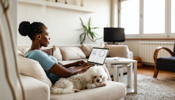 A woman sits on a couch and works on her computer at home.