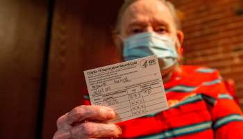 An man holds up his COVID-19 vaccine certificate.