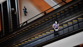 A woman stands on an escalator, wearing a mask.