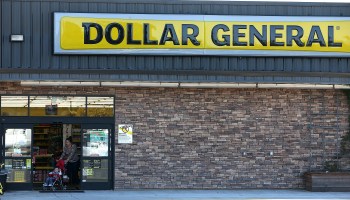 A customer pushing a child in a stroller leaves a Dollar General store.