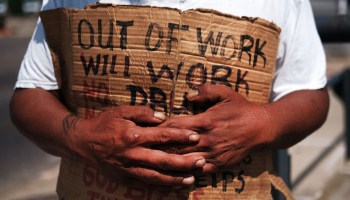A person holds a sign reading "Out of work, will work."