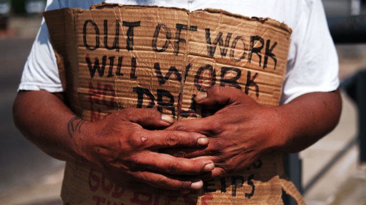 A person holds a sign reading "Out of work, will work."