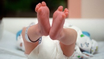 A baby in diapers lies on its back, its feet in the air.