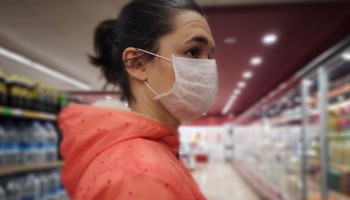 A young woman wearing a mask stands in the grocery store.