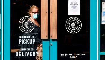 A woman wearing a facemask exits a Chipotle Mexican Grill restaurant with her takeout order.