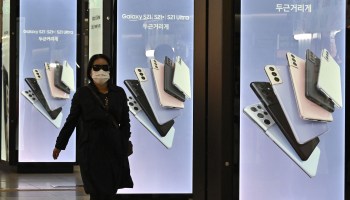 This picture taken on April 28, 2021 shows a woman walking past an advertisement for the Samsung Galaxy S21 smartphone at an underground shopping area in Seoul, South Korea..