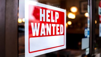 A "Help Wanted" sign is posted on a store window.