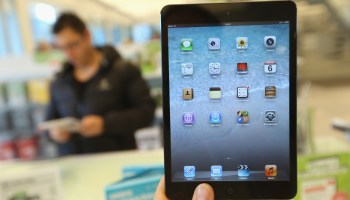 A photographer holds up an Apple iPad Mini at a display table.