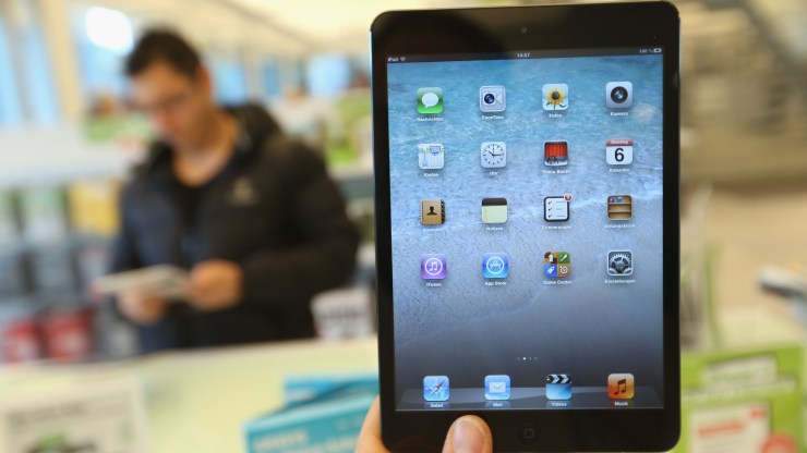 A photographer holds up an Apple iPad Mini at a display table.