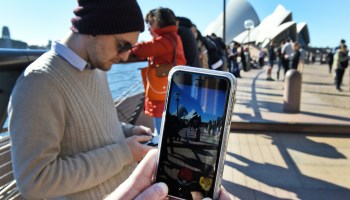 A man holds up his smartphone, which displays the "Pokemon Go" app, in front of the Sydney Opera House, on July 15, 2016.