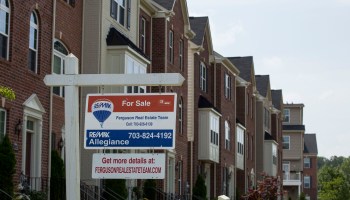 A "For Sale" sign hangs in front of a row of homes.